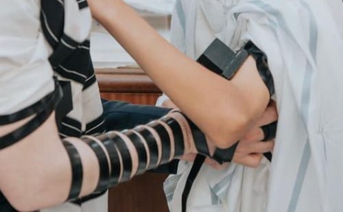 הנחת תפילין - יד מלפפת את הרצועה על זרועו של נער