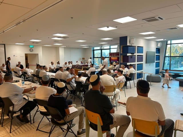קהל מתפללים באולם, יושבים סביב השולחנות